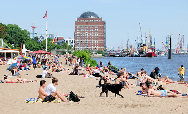 7297 Strandszene in Hamburg Othmarschen - Menschen liegen im Sand in der Sonne am Ufer der Elbe - im Hintergrund das ehem. Kühlhaus von Neumühlen und der Museumshafen mit historischen Schiffen.