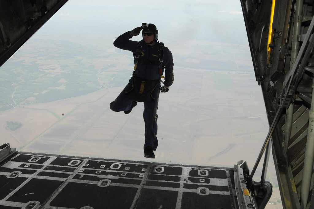 A U.S. Navy parachute demonstration team member salutes as he steps off the ramp of a C-130 Hercules aircraft.
