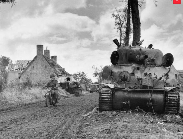 A motorcycle despatch rider passes a knocked-out Sherman tank and behind, a German Panther at Fontenay-le-Pesnel, 27 June 1944
