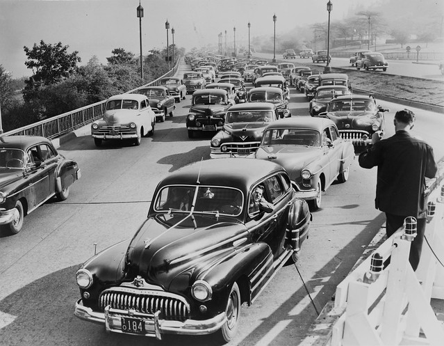 Lots of rounded 1940s cars with split windshields and incredibly large chrome bumpers stuck in traffic going southbound on the West Side Highway at the 72nd street exit. Look at those fenders! New York. 1953