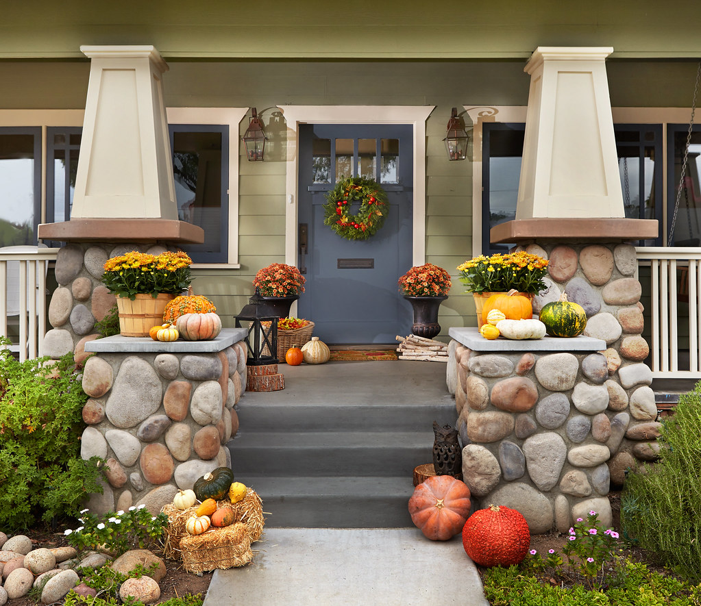 Front porch and doorstep decorated for fall with flowers, pumpkins and other squash and a wreath