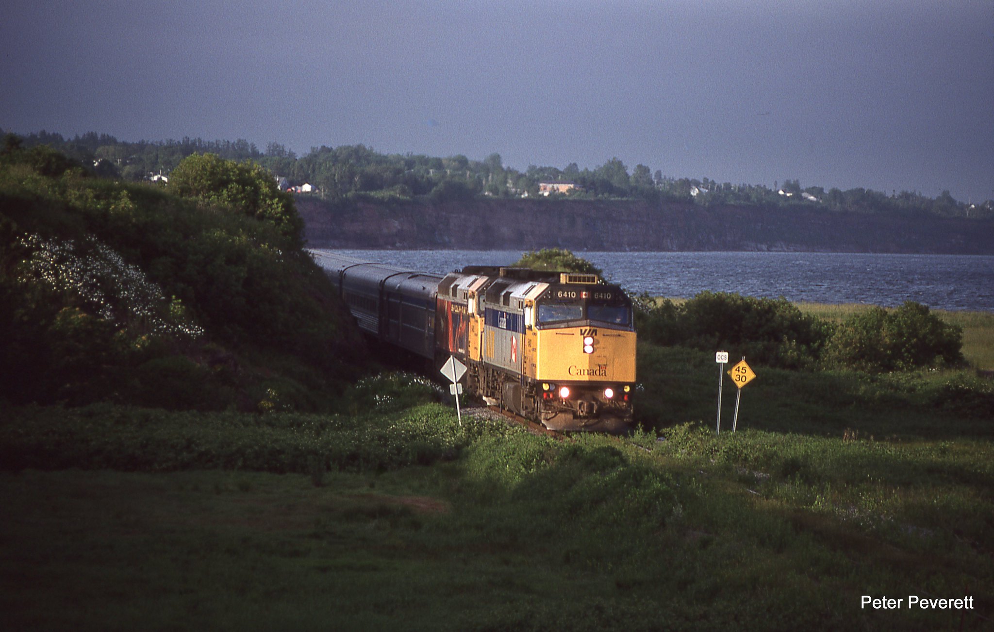 The westbound VIA Train the Chaleur with F40PH-2 # 6410, 6408 has found a small spot of remaining sun at New Carlisle, Quebec June 28, 2008. The train is slowing for the station stop and crew change.  New Carlisle has a small yard and wye left from the CN days which is now overgrown .  It has finished the run on the Chandler Sub. and will finish in Matapedia, the end of the Cascapedia Sub.  Sadly this far out no trains operate at this time.   