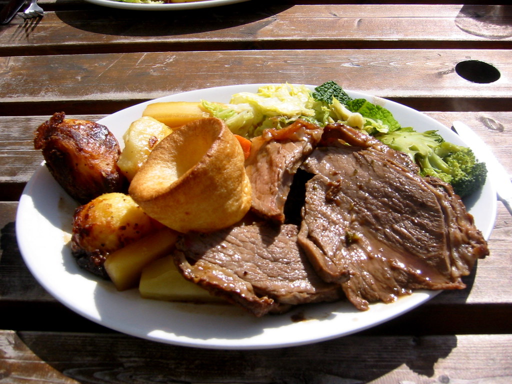 Plated roast dinner with sliced beef, roasted potatoes, Yorkshire pudding, and greens`