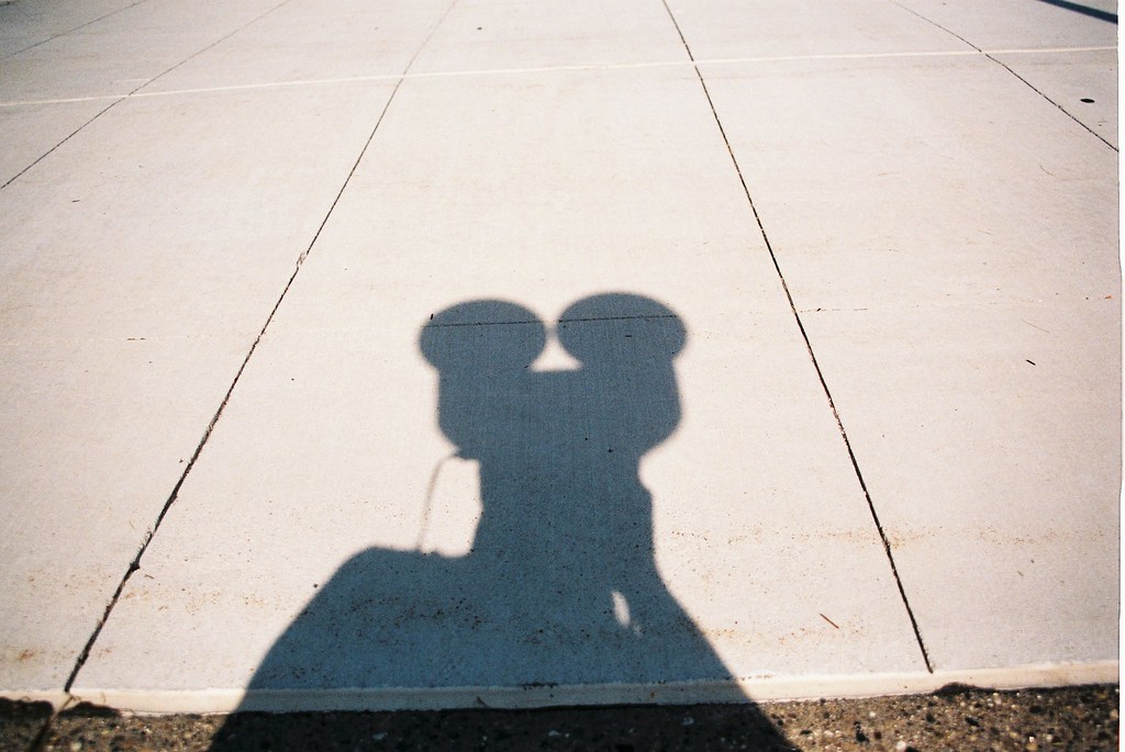 Photographer's shadow on a sunlit Detroit sidewalk forming a silhouette resembling Mickey Mouse ears.