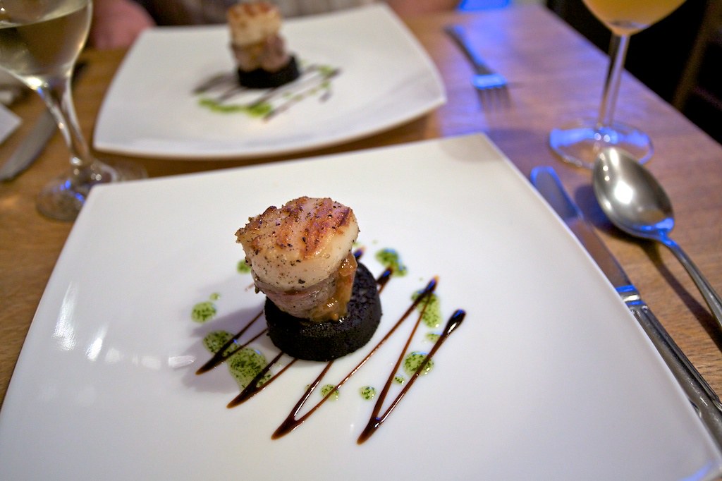 Elegant seared scallop dish with herb garnish and sauce drizzle on a white plate at a fine-dining table