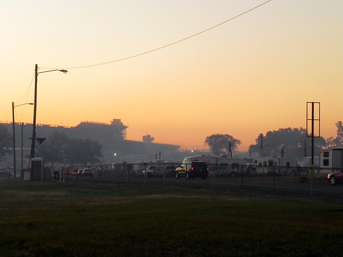Looming by Clint Midwestwood, The haze-shrouded stands of Talladega Motor Speedway loom in the distance as early birds start filin