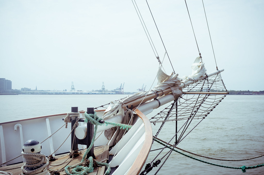 View from the wooden bow of a sailing schooner across New York Harbor with canvas sails and bowsprit.