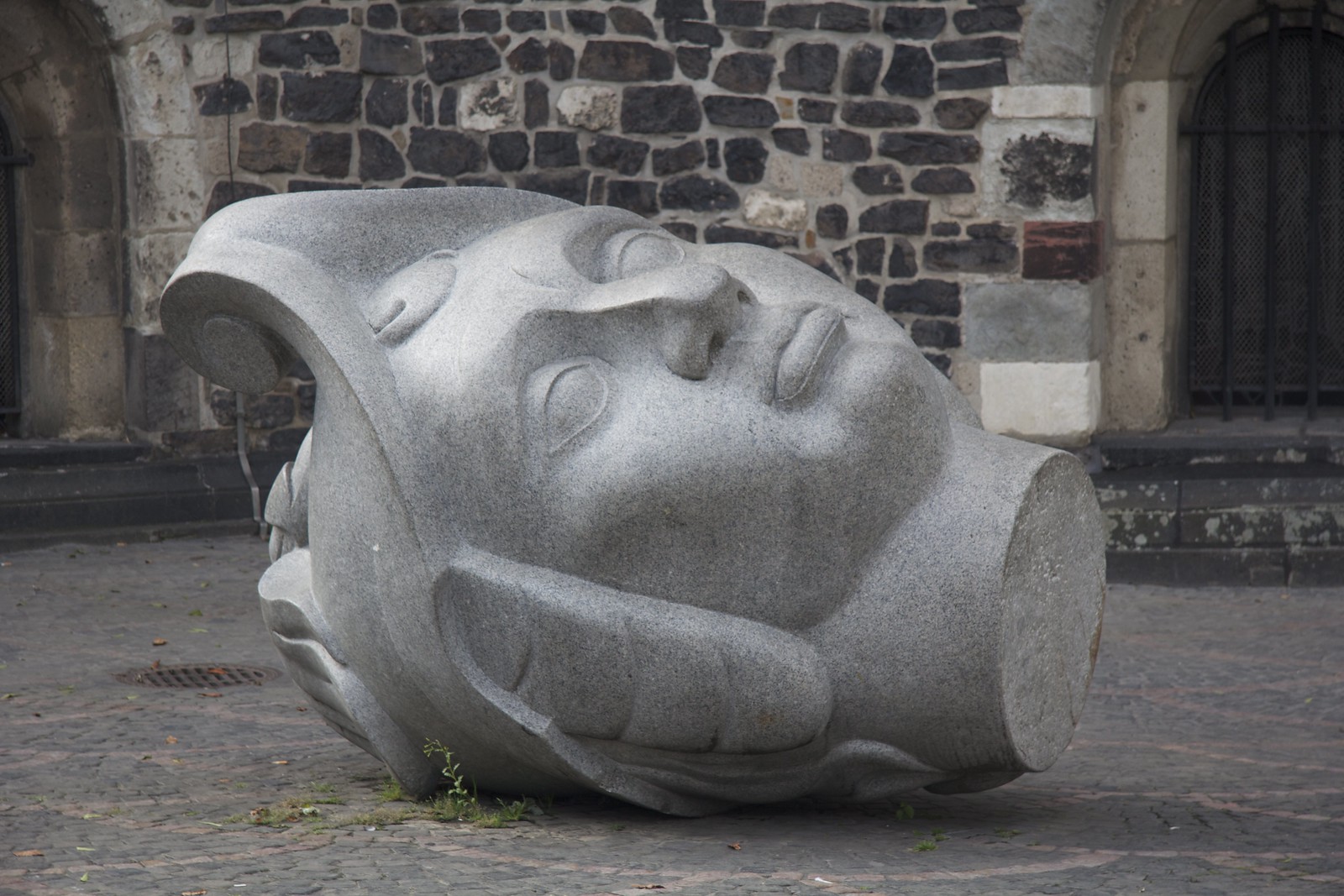 Gray stone sculpture depicting the fallen head of a larger statue