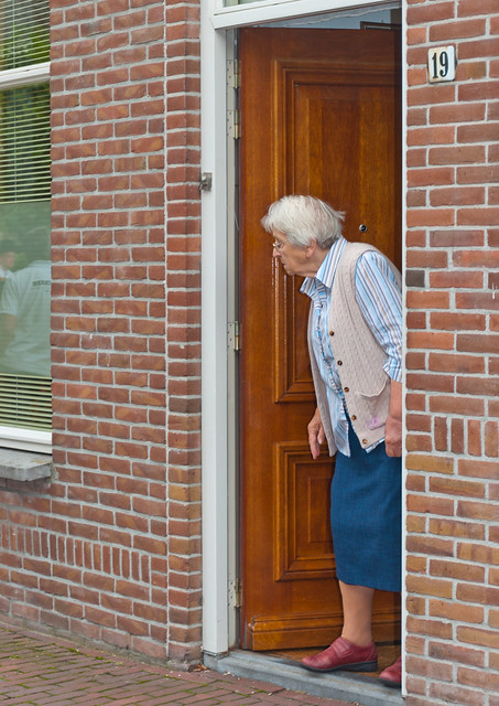 Oude vrouw kijkt uit de voordeur - Old woman looks from her front door