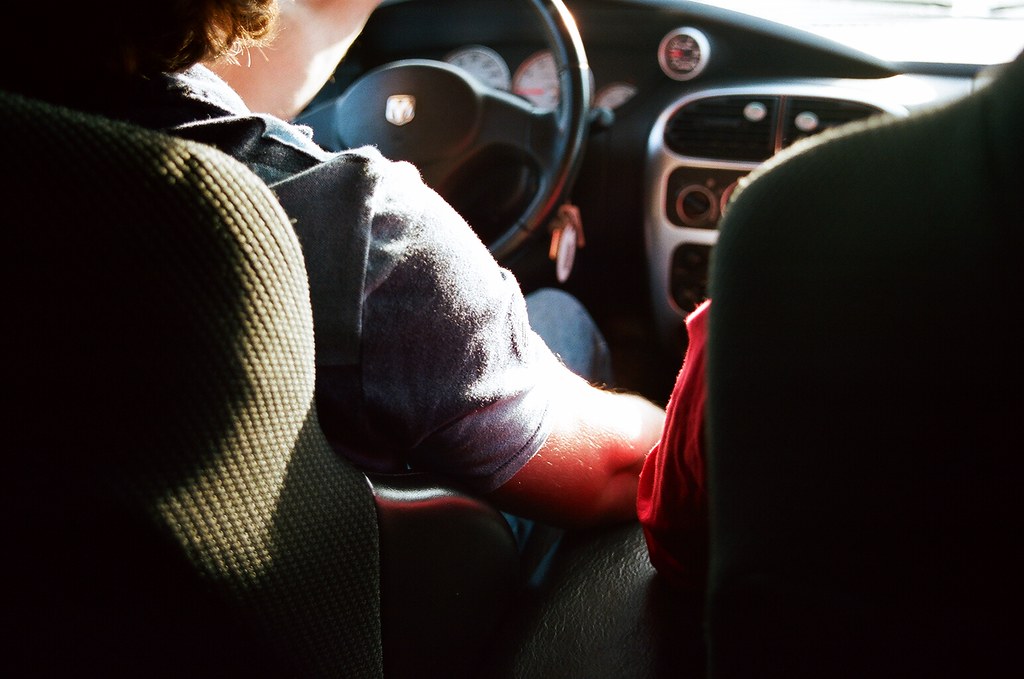 Sunlit view looking over the shoulder of a driver gripping the steering wheel on a road trip in Detroit.
