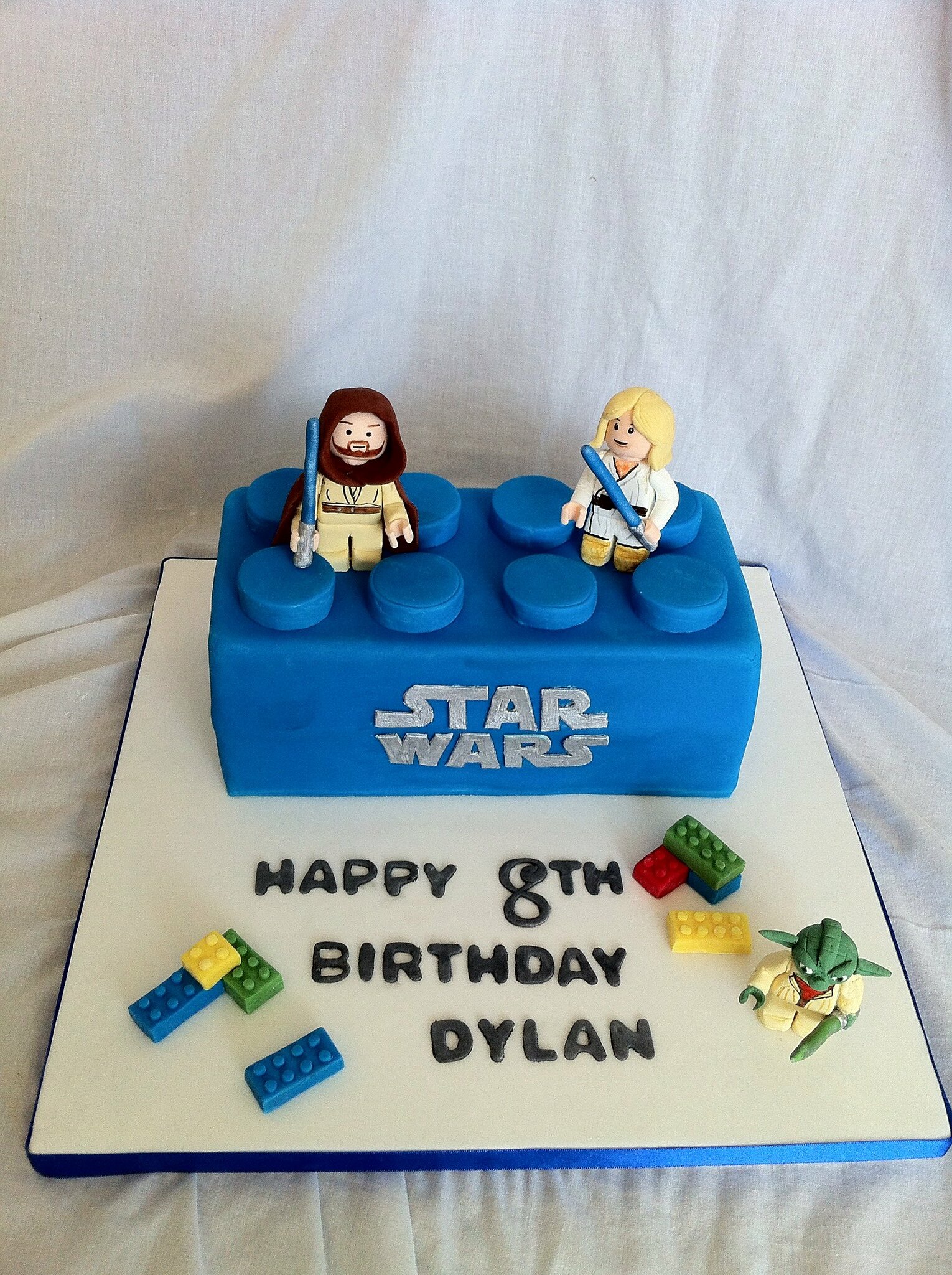 A blue LEGO brick cake with a couple of fondant LEGO Star Wars Minifigures on top