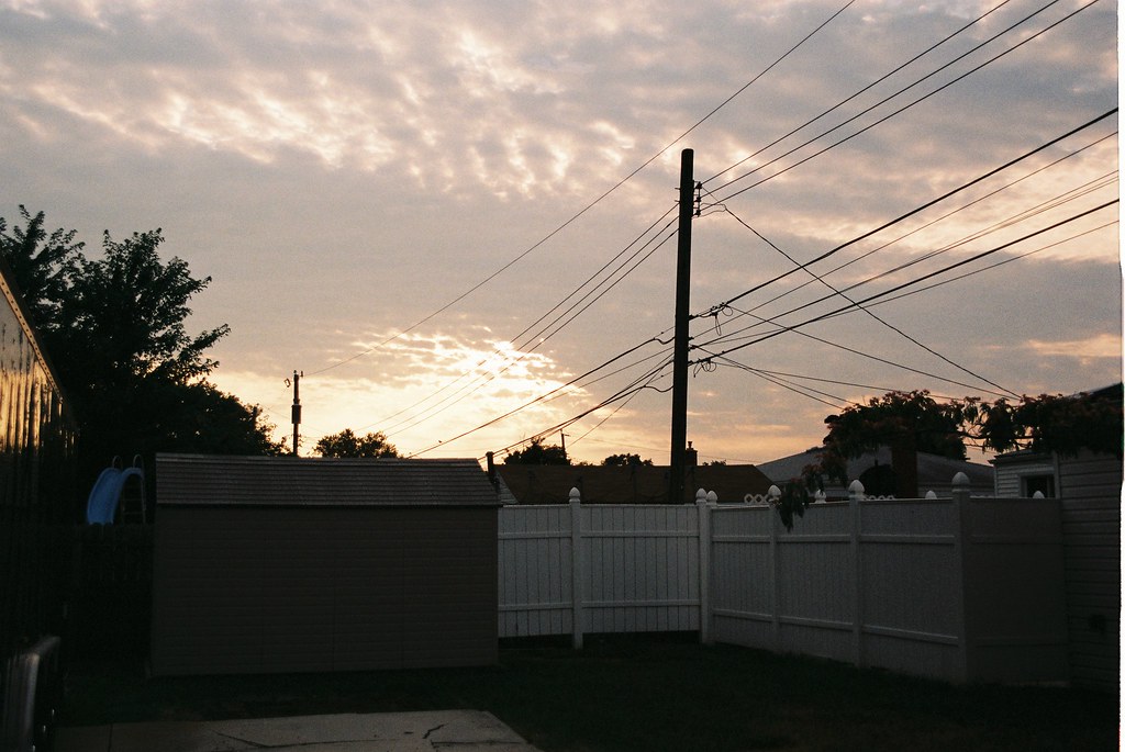 Suburban Michigan backyard at sunset with a garden shed and white vinyl fence beneath rippling clouds.
