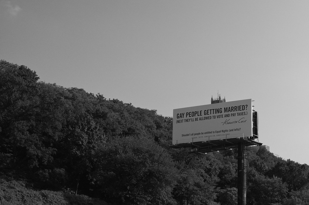Kenneth Cole billboard advocating for marriage equality beside a wooded hillside along a highway.