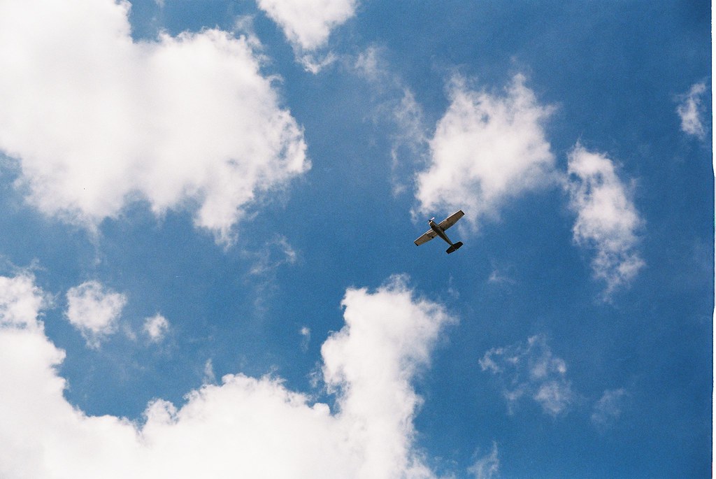 Single-engine propeller airplane soaring through puffy white clouds in a blue summer sky over Michigan.