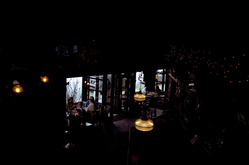 High-angle view into a dimly lit tavern with warm amber globe lights and patrons seated at wooden tables.