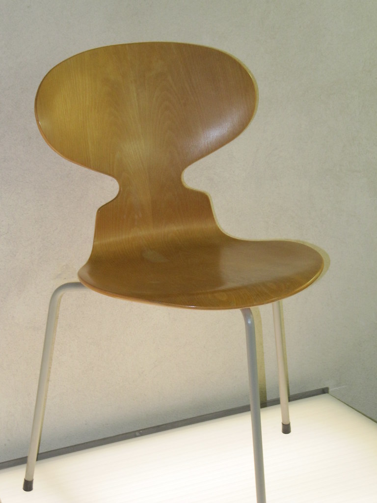 Ant chair 00: A light brown wood chair with three legs. 