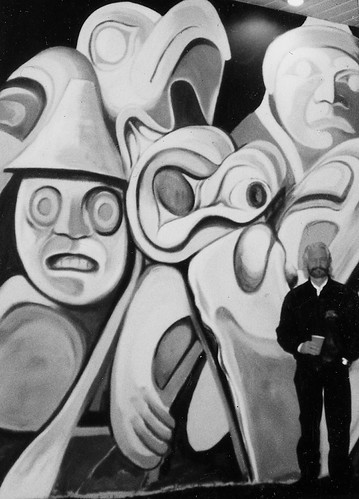 Artist beside a mural of carved mask forms