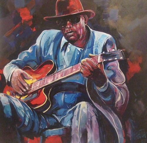 Seated guitarist wearing a hat and blue shirt