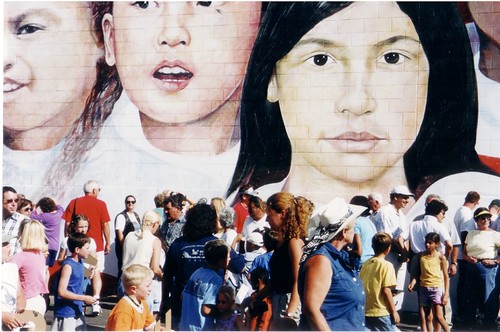 Crowd gathered below a mural of children's faces