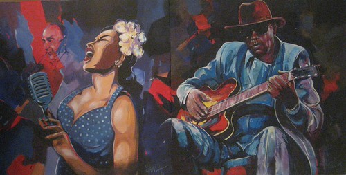 Singer beside a seated guitarist wearing a hat