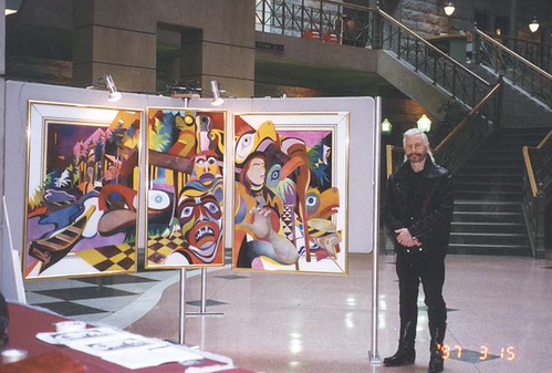 Artist beside a framed multi-panel mask composition