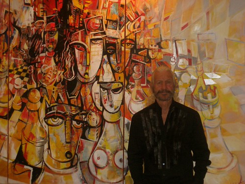 Artist standing beside a large chess-themed painting