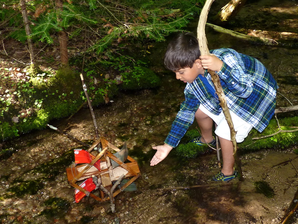 A child tests a model waterwheel in a park creek.