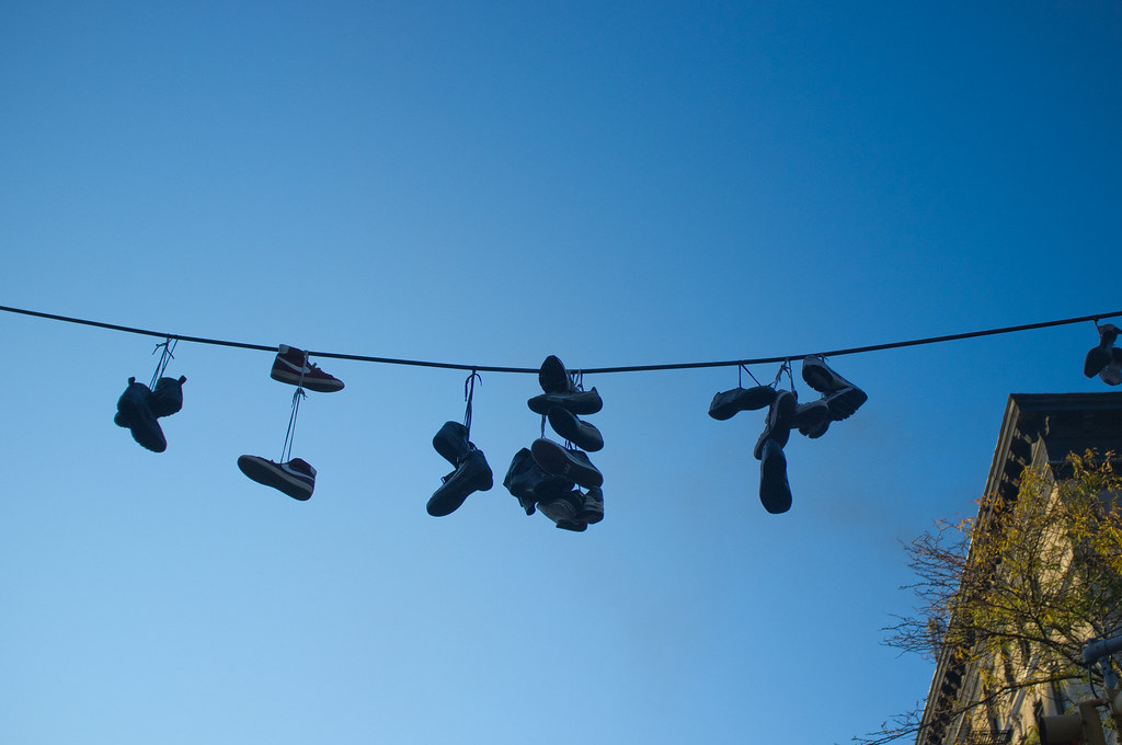 Sneakers and work boots dangling by their laces from an overhead utility cable in New York City.