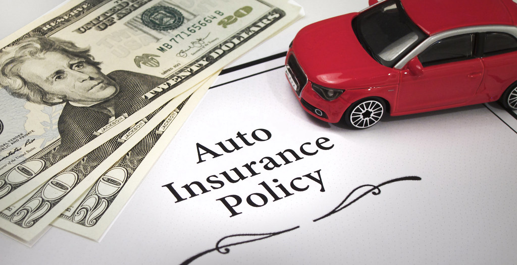 Toy car and three, $20 bills on top of an Auto Insurance Policy