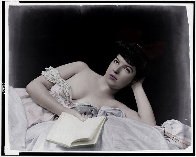 Young woman, wearing negligee, lying in bed, holding book