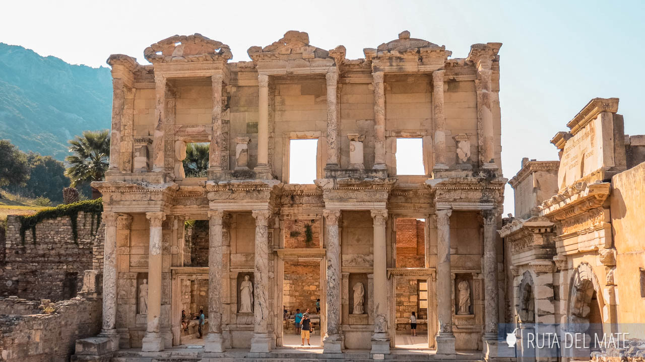 In the foreground is the Library of Ephesus. It is only the two-story façade standing, light-colored, with its columns and statues. There are people hanging around.