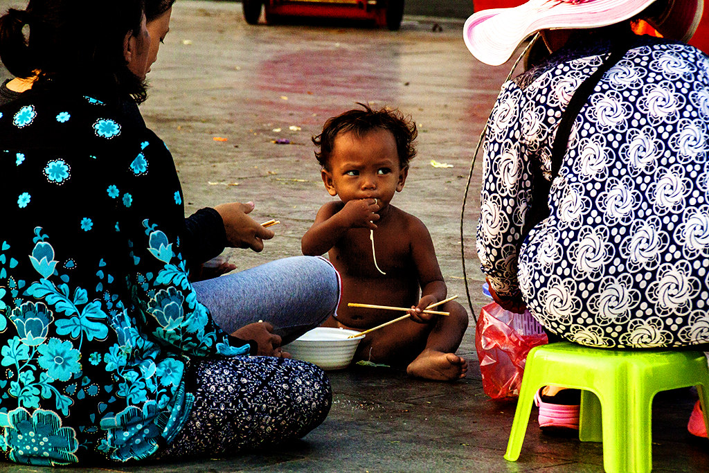Naked boy sitting on ground eating noodles--Phnom Penh