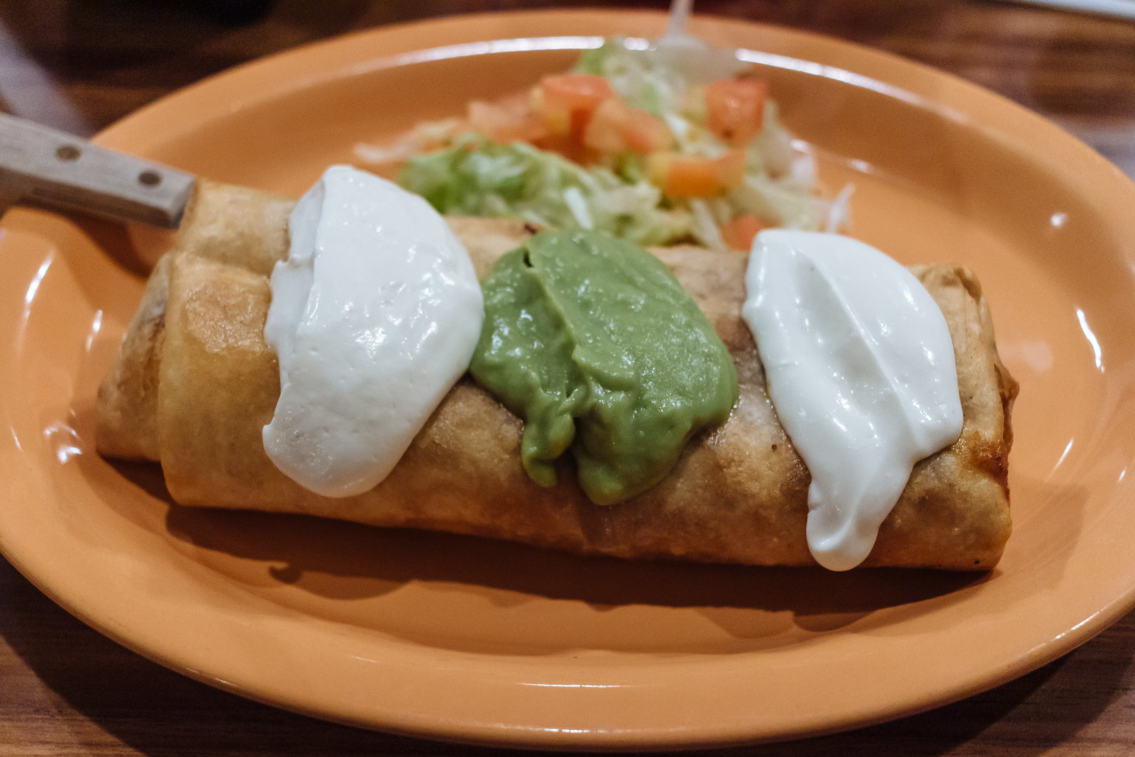 A chimichanga or deep-fried burrito topped with dollops of sour cream and guacamole