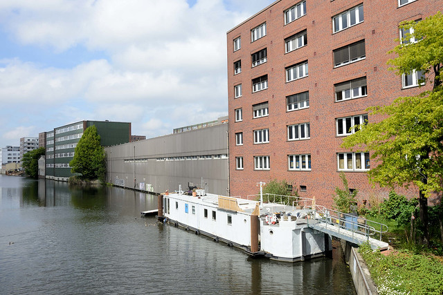 7718 Fotos aus dem Hamburger Stadtteil Hamm - Bezirk Mitte. Blick von der ersten Grevenbrücke / Grevenweg auf einen Wohnblock mit Balkons und Gewerbegebäude am Mittelkanal, ein Industriekanal von Hamburg-Hamm; ein Hausboot liegt am Kanalufer.