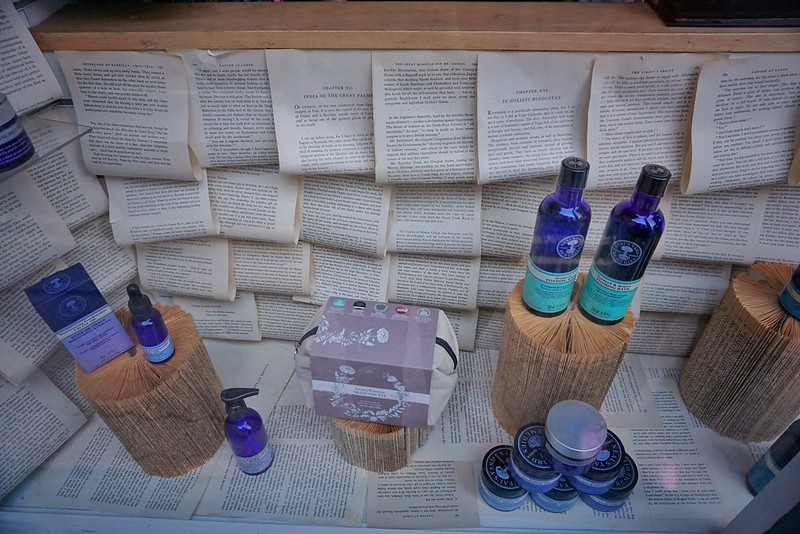A window display of folded book pages and glass bottles in a pharmacy