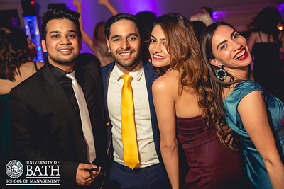 Four people at a formal event smiling. They are dressed in formal clothing and look to be having a good time. 