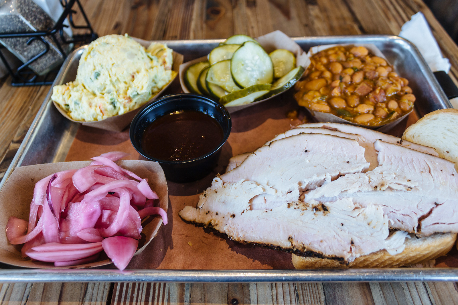 Tray with slices of barbecue turkey meat, pickled red onions, potato salad, pickles, and beans