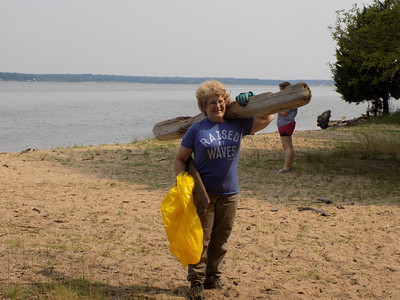 A volunteer carries a bag of trash and a board off the beach.