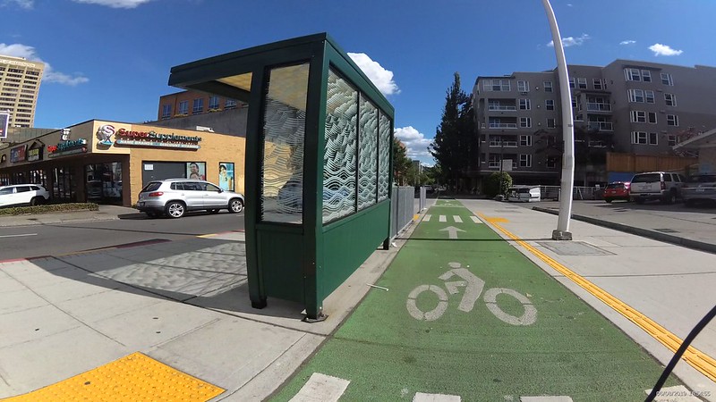 A raised green painted bike lane next to a bus shelter on the let.