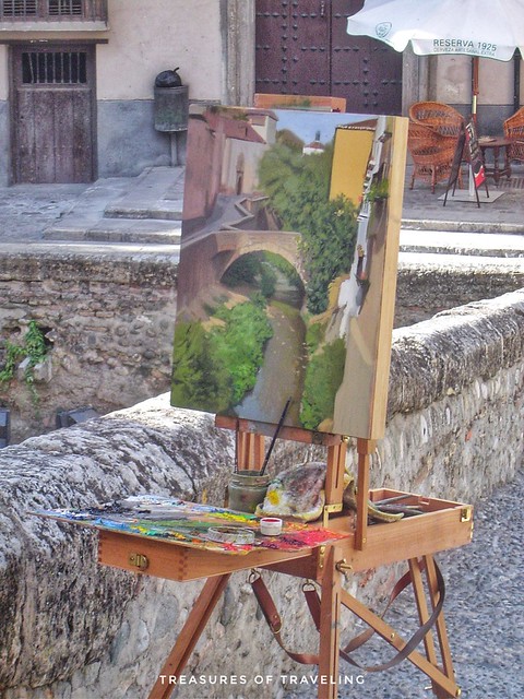 An artist painting a beautiful river scene from along the Carrera del Darro, which is a road that runs along the Darro River in the Albaicín. As you walk along the road don't forget to look up to see the Alhambra, which sits on top of the hill right acros
