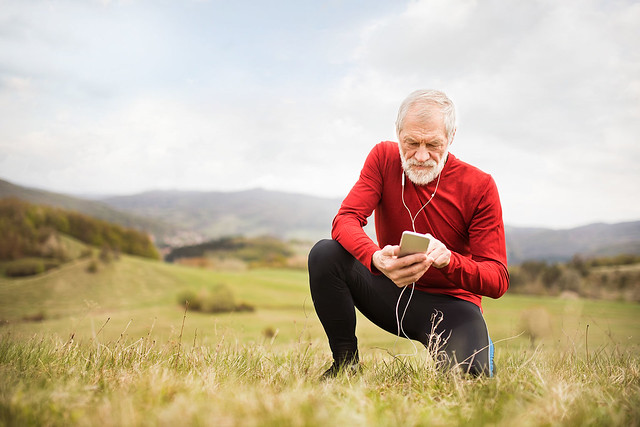 Active senior runner in nature with smart phone and earphones.