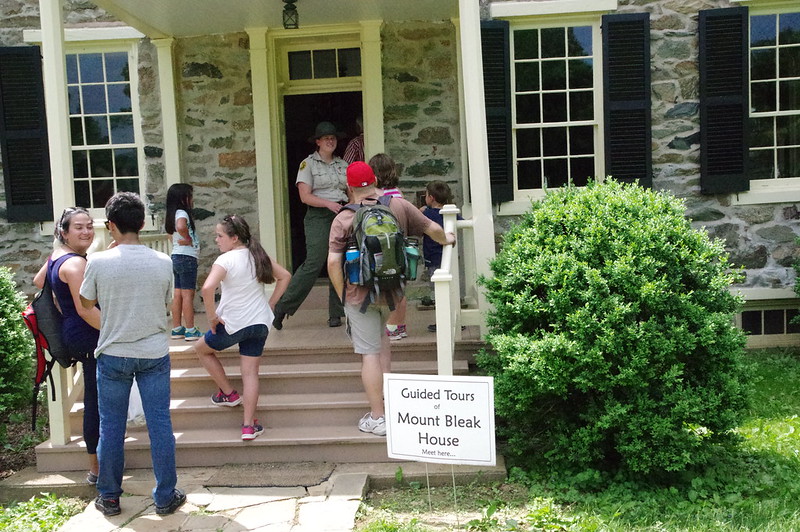 A group of people around the front steps of a stone house with a Park Ranger and a sign that reads: Guided Tours of Mount Bleak House