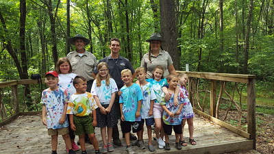 Rangers and Junior Rangers smile from an outdoor wooded stage.