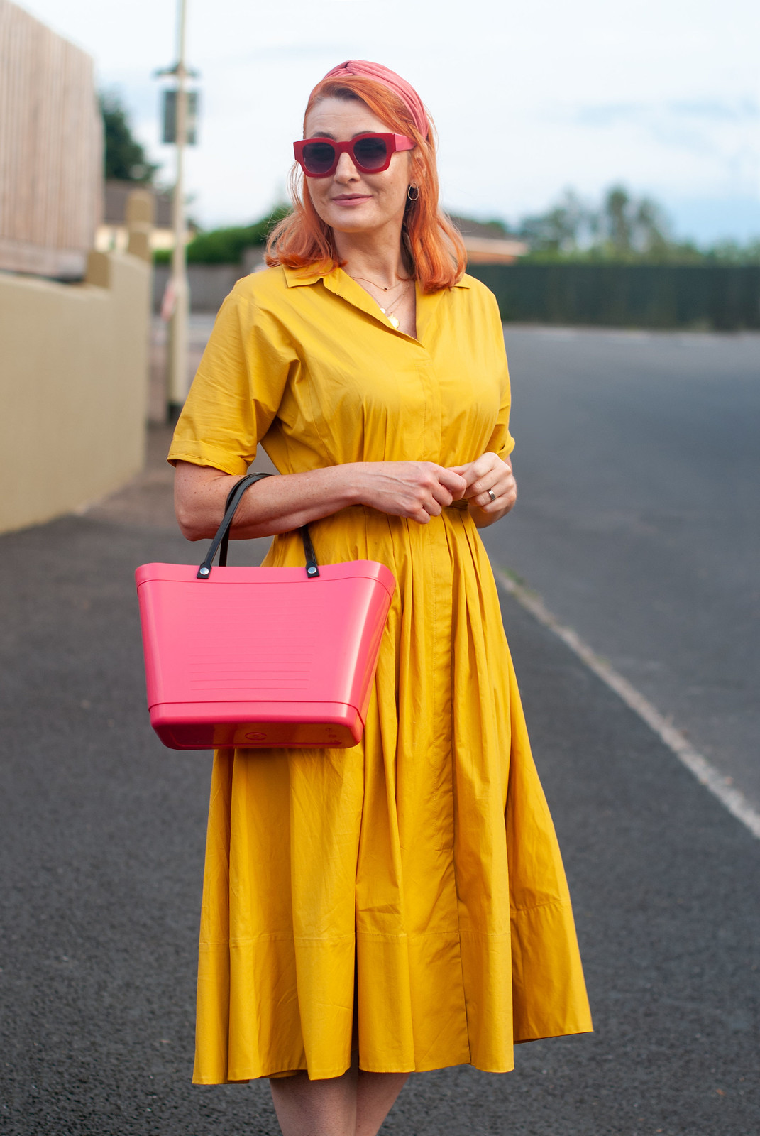 Over 40 fashion blogger Not Dressed As Lamb wearing a yellow summer dress in a shirt style \ red strappy block heels \ pink bucket bag \ pink headband \ red square sunglasses