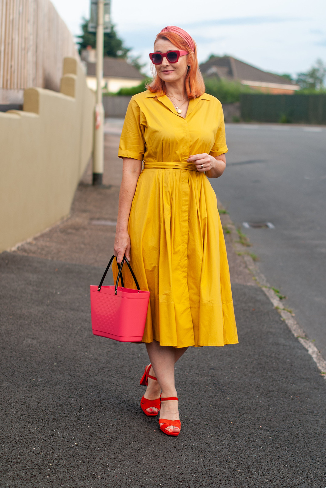 Over 40 fashion blogger Not Dressed As Lamb wearing a yellow summer dress in a shirt style \ red strappy block heels \ pink bucket bag \ pink headband \ red square sunglasses