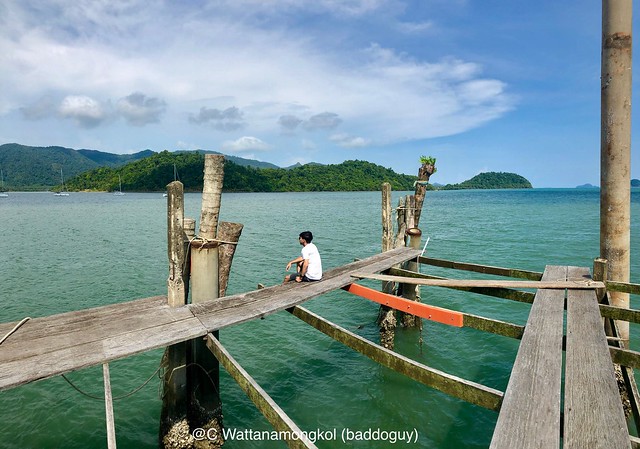 Ko Chang Scenery - A man is sitting on the wooden pier looking at view of Ao Salak Phet Bay in a sunny day with blue sky and white cloud.