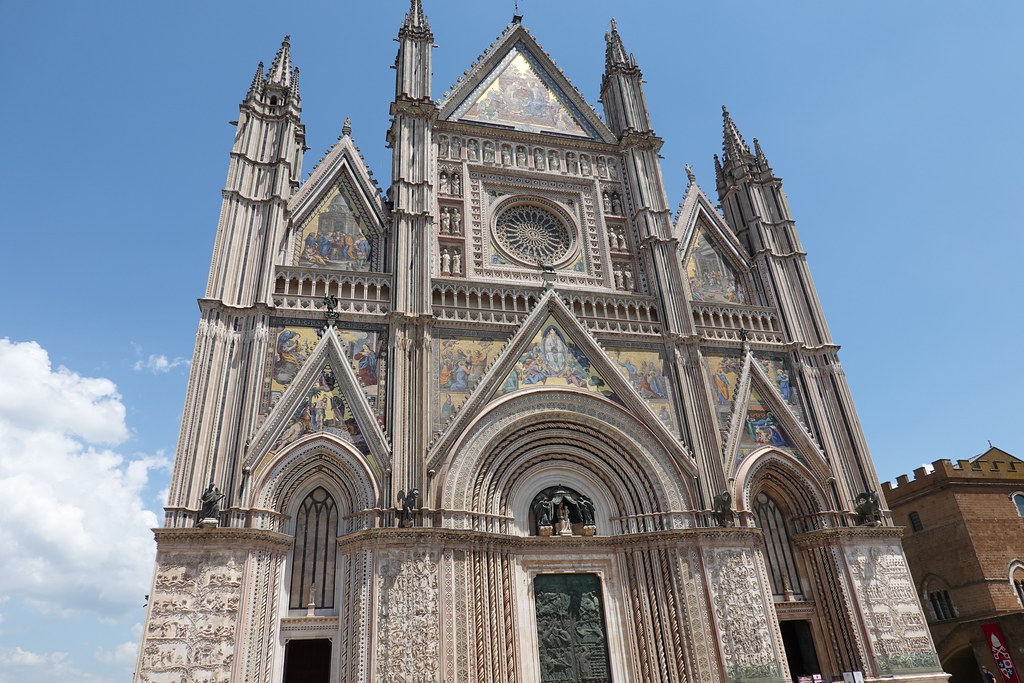 Facade of Orvieto Cathedral: A large, ornate grey stone structure with various arches and triangular points. 