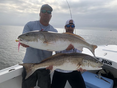 Photo of two men as they hold up a pair of red drum.