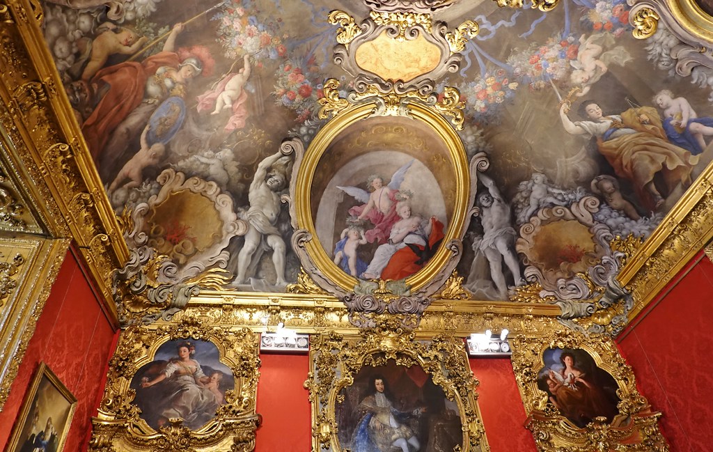 Bedchamber of Madame Real, 1708-1709; Palazzo Madama, Turin (4). Picture of the ceiling art with various angels and warriors. Moreover, gold ornaments line the entire photo and the tops of the walls are a stark, red color.  