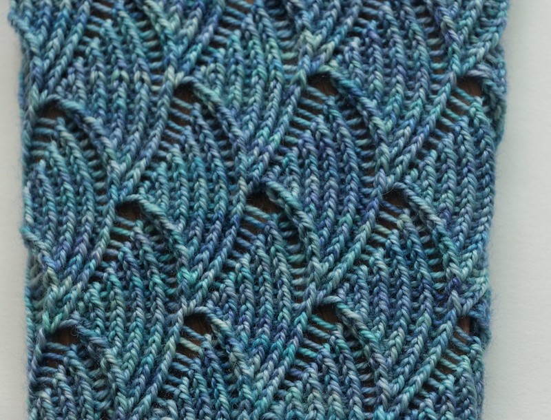 Detail view of handknit Pomatomus socks on sock blockers, showing lace pattern in SweetGeorgia Mermaid yarn